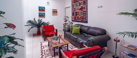 A living room with a sofa, armchair, coffee table, and potted plants.