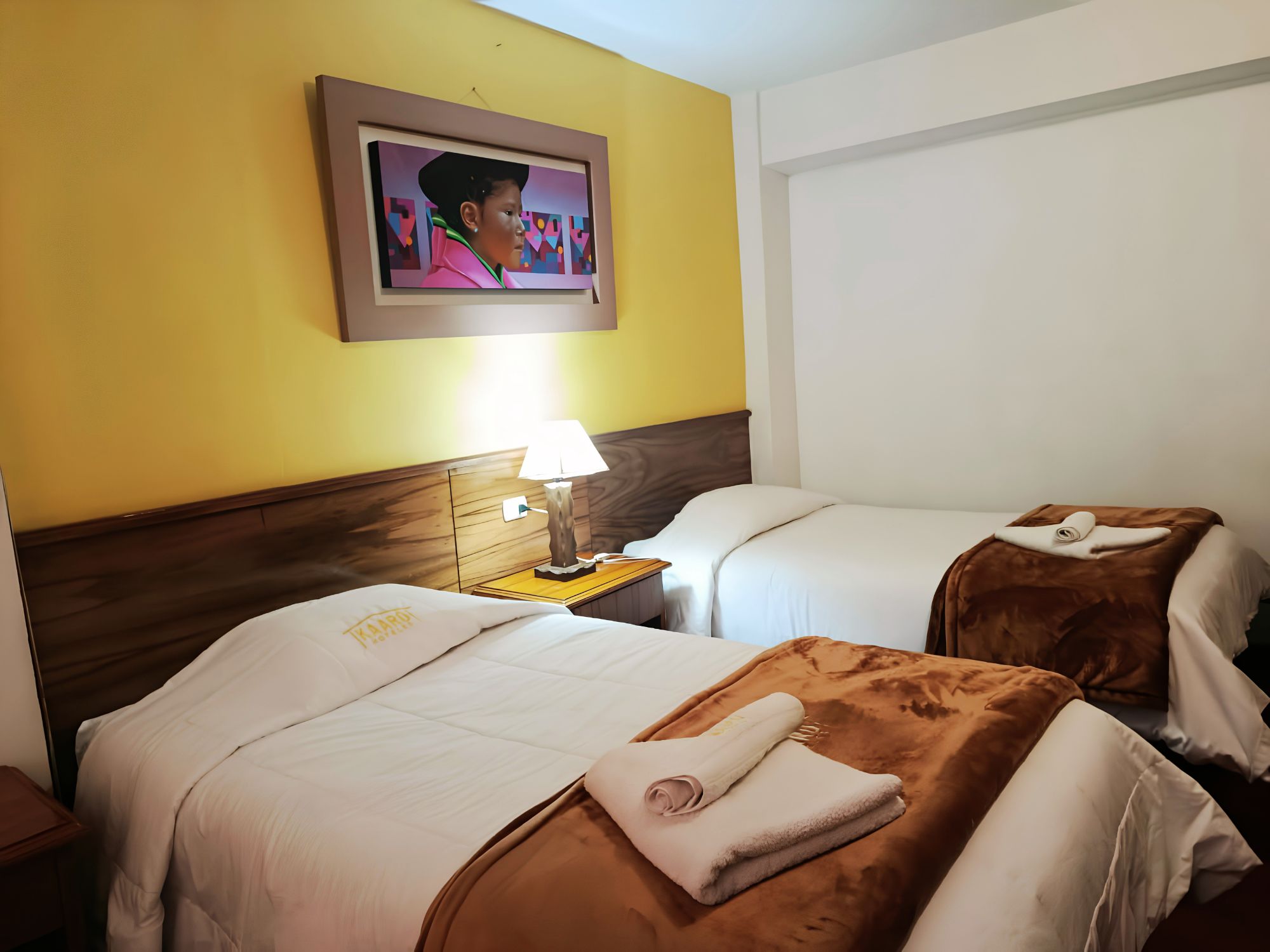 Una habitación de hotel con dos camas, una mesita de noche con una lámpara y un cuadro en la pared.
