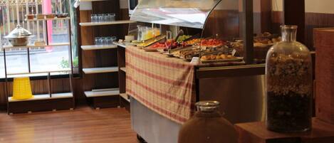 A buffet area with a variety of food items, a glass jar, and a metal container on a wooden counter.