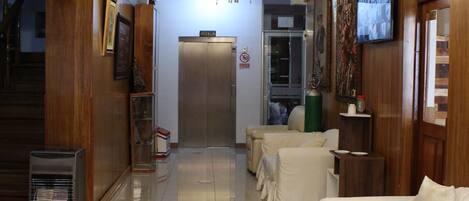 Un hall de hotel con una araña, una recepción, una escalera y una fila de sofás blancos.