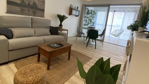 A modern living room with a sofa, coffee table, and a dining area with chairs. - Sète! 50m2 new parking wifi quay Town center (Sète)