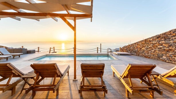 A poolside area with wooden loungers and a stone wall, overlooking a body of water during sunset. - Live In Blue - Uranian Private Pool & Magic Views (Coressia)