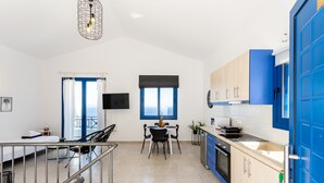 A modern kitchen with blue cabinets, a dining area with a table and chairs, and a large window with a view. - Live In Blue - Uranian Private Pool & Magic Views (Coressia)