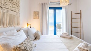 A bedroom with a bed, pillows, a macrame wall hanging, a ladder, and a view of the outdoors. - Live In Blue - Uranian Private Pool & Magic Views (Coressia)
