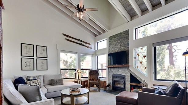 A spacious living room with a fireplace, large windows, and a ceiling fan. - Summer Fun - SLOPESIDE 4BR/3BA with 3 Spas, Pool and Sauna - Perfect for Family and Friend Getaways All Year Round by RedAwning (Mammoth Lakes)