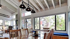A spacious dining area with a long wooden table, multiple chairs, and large windows offering a view of the outdoors. - Summer Fun - SLOPESIDE 4BR/3BA with 3 Spas, Pool and Sauna - Perfect for Family and Friend Getaways All Year Round by RedAwning (Mammoth Lakes)