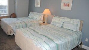 Quarto com duas camas, uma mesa de cabeceira com abajur e quadros nas paredes.
