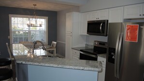 A kitchen with white cabinets, a stainless steel refrigerator, a microwave, and a stove.