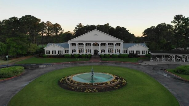 A large, symmetrical building with a central fountain, surrounded by well-manicured lawns and trees.