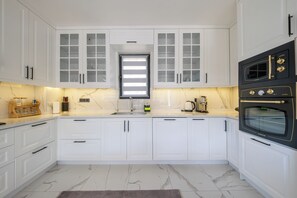 A modern kitchen with white cabinetry, a black oven, and a marble countertop. - Olive Hills Villa Family-Friendly Luxury Villa with Private Pool in Fethiye (Fethiye)