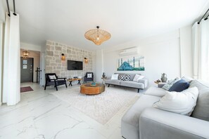 A modern living room with a stone wall, a flat-screen TV, a grey sofa, and a coffee table. - Olive Hills Villa Family-Friendly Luxury Villa with Private Pool in Fethiye (Fethiye)