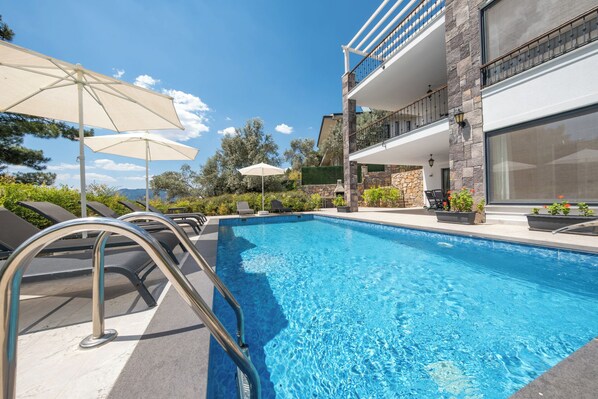A swimming pool with a metal ladder, lounge chairs, and umbrellas. - Olive Hills Villa Family-Friendly Luxury Villa with Private Pool in Fethiye (Fethiye)