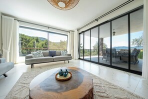 A spacious living room with a large sliding glass door leading to an outdoor patio area. - Olive Hills Villa Family-Friendly Luxury Villa with Private Pool in Fethiye (Fethiye)