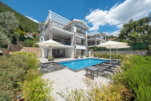 Ein mehrstöckiges Haus mit Swimmingpool, Gartenmöbeln und einer Steinmauer.