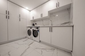 A modern laundry room with two front-loading washing machines, white cabinetry, and a marble backsplash. - Olive Hills Villa Family-Friendly Luxury Villa with Private Pool in Fethiye (Fethiye)