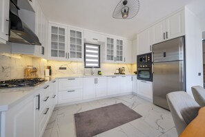 Une cuisine moderne avec des meubles blancs, un réfrigérateur en acier inoxydable, un four encastré et une cuisinière à gaz.