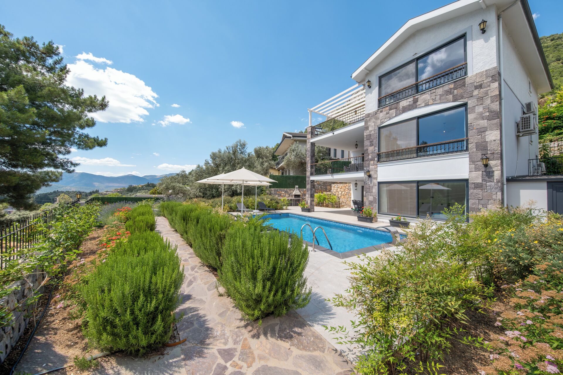 A modern two-story house with a swimming pool, stone pathway, and lush greenery.