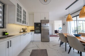 A modern kitchen with white cabinetry, a stainless steel refrigerator, and a dining area with a table and chairs. - Olive Hills Villa Family-Friendly Luxury Villa with Private Pool in Fethiye (Fethiye)