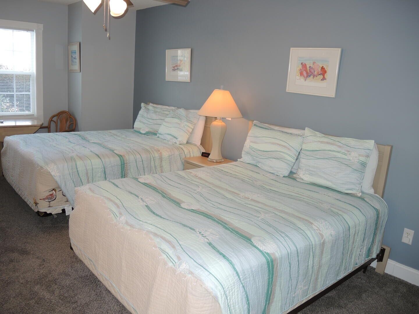 A bedroom with two beds, a nightstand with a lamp, and framed pictures on the wall.