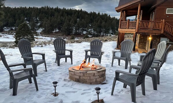 Relax in a serene outdoor seating area surrounded by a forest, featuring a fire pit and a balcony with a scenic view.