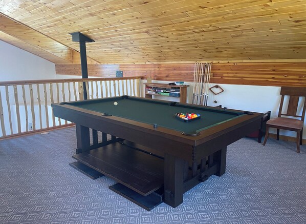 Une table de billard dans une pièce aux murs en bois et au plafond en pente.