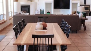 Een eetgedeelte met een houten tafel en stoelen, een open haard, een televisie en een bank op de achtergrond.