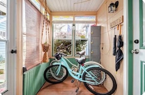 A narrow room with a bicycle, a wooden door, and a view through a window.