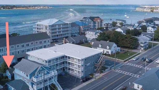 Une ville côtière qui se distingue par un imposant bâtiment situé en bord de mer, doté de plusieurs étages et de balcons, ainsi que d’un espace de stationnement et offrant une vue dégagée sur la mer.