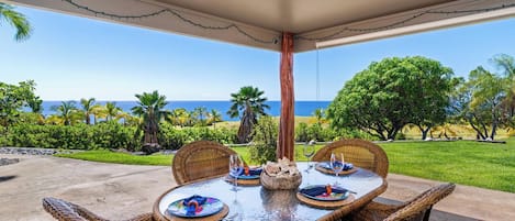 An outdoor dining area with a view of the ocean, wicker furniture, and a table set for two.