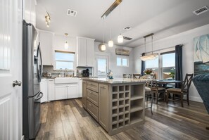 Una cocina moderna con armarios blancos, una isla grande con espacio para vinos e iluminación colgante.