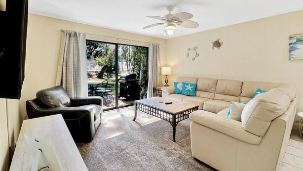 A living room with a beige sofa, a black leather chair, a coffee table, and a ceiling fan. - Charming Pet Friendly Villa - Steps to the Beach and Coligny Plaza! (Hilton Head Island)