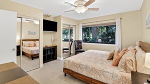A bedroom with a bed, a TV, a ceiling fan, and a window with a view of trees. - Charming Pet Friendly Villa - Steps to the Beach and Coligny Plaza! (Hilton Head Island)