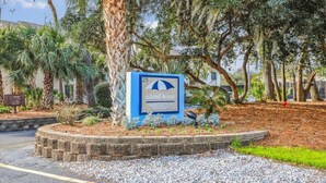 A sign for 'Island House' with a beach umbrella symbol, surrounded by trees and a landscaped area. - Charming Pet Friendly Villa - Steps to the Beach and Coligny Plaza! (Hilton Head Island)