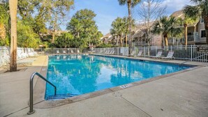 A rectangular pool with a metal ladder on the left, surrounded by palm trees and a white fence. - Charming Pet Friendly Villa - Steps to the Beach and Coligny Plaza! (Hilton Head Island)