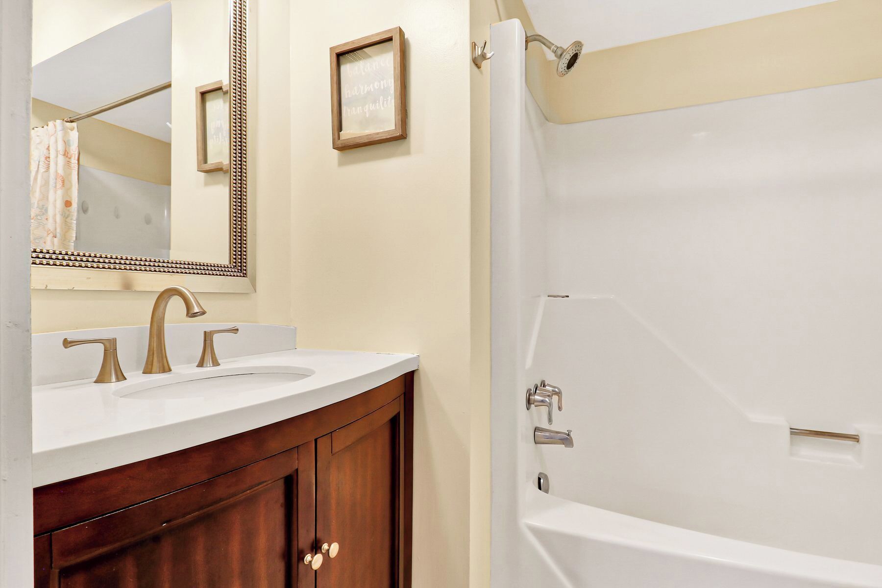 Un bagno con una vasca da bagno bianca, due lavandini con rubinetti dorati, un mobile bagno in legno e uno specchio con cornice decorativa.
