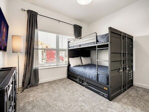 A compact room with a bunk bed, a desk, a lamp, and a window with curtains.