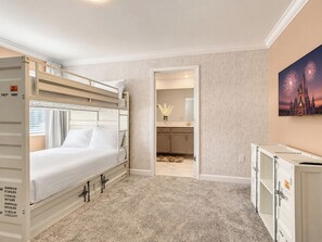 A hotel room with a bunk bed, a bathroom with a mirror, and a painting of fireworks.