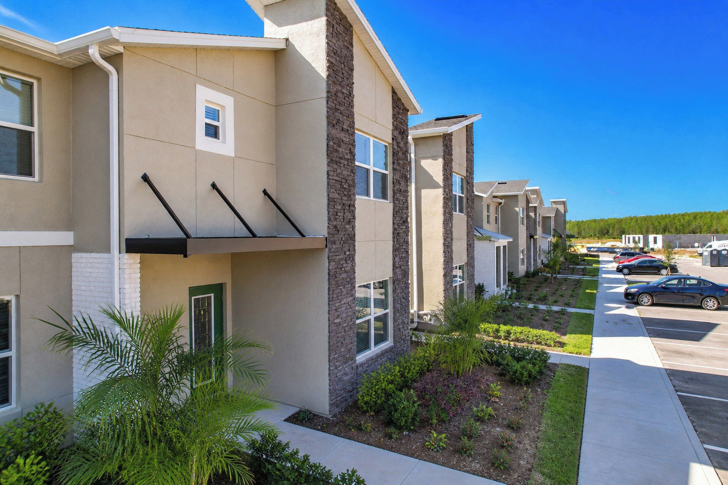 A row of modern apartment buildings with a parking lot and green landscaping.