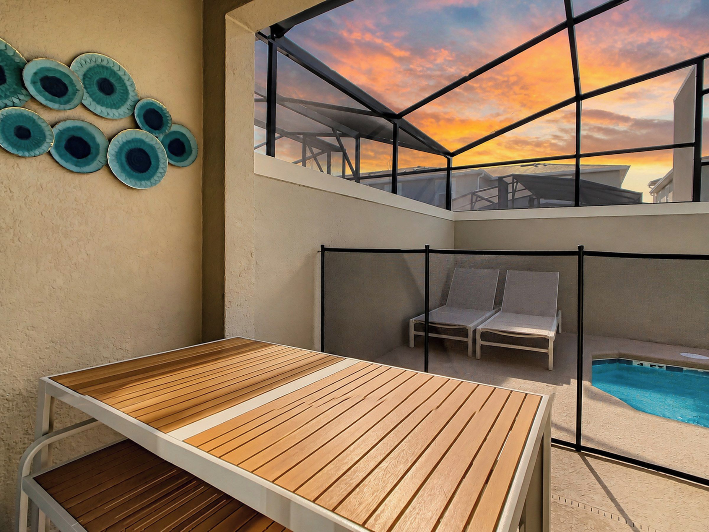 Un espace extérieur ensoleillé avec une table en bois, des chaises longues et une piscine.