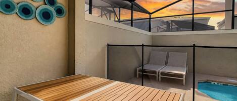 Un espace extérieur ensoleillé avec une table en bois, des chaises longues et une piscine.