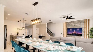 A dining area with a long table set for a meal, a ceiling fan, and a wall-mounted TV displaying fireworks.