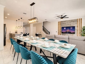 A dining area with a long table set for a meal, a ceiling fan, and a wall-mounted TV displaying fireworks.