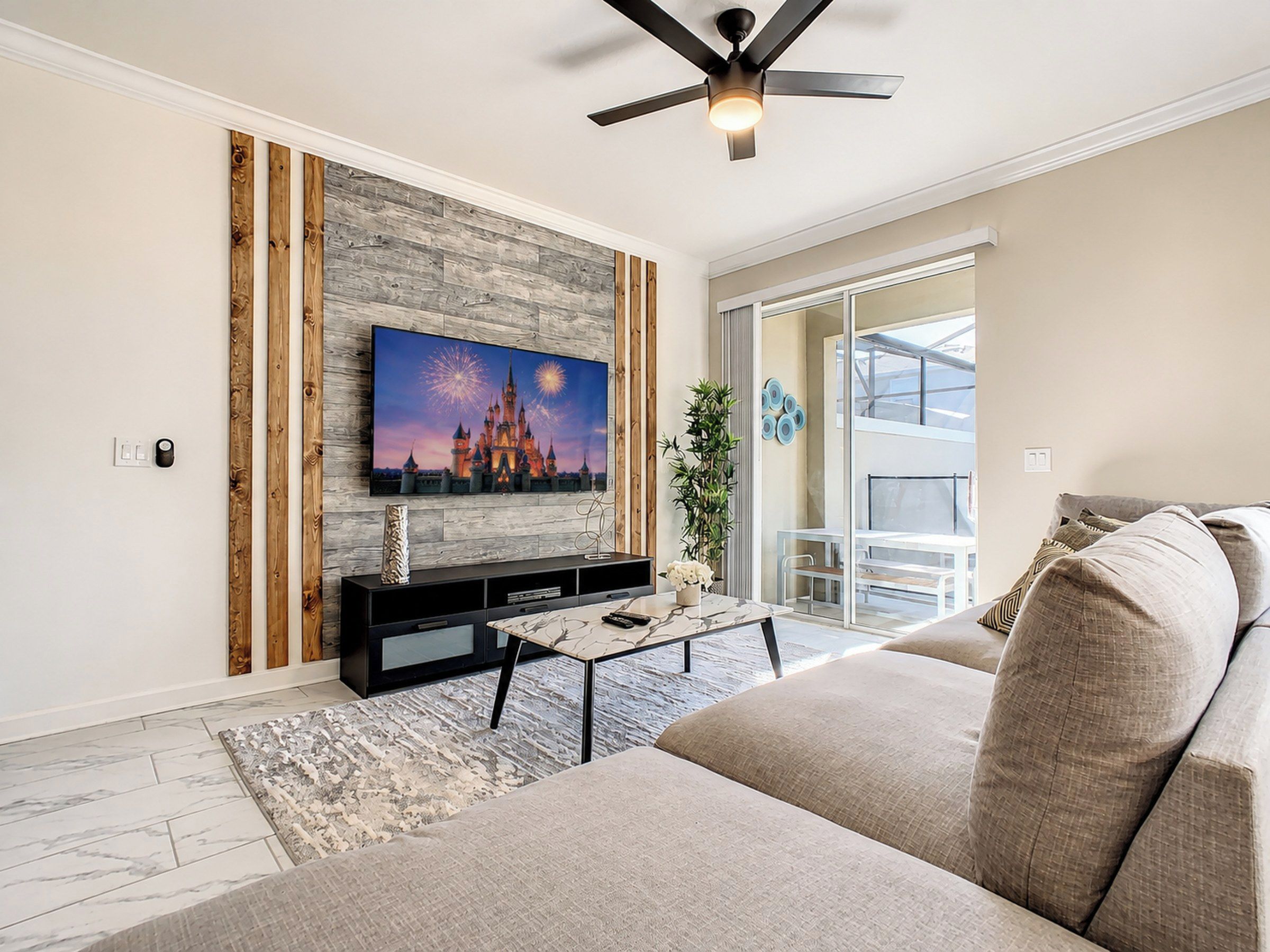 A modern living room with a flat-screen TV mounted on a textured wall, a ceiling fan, a sofa, and a coffee table.