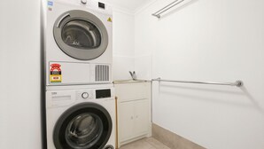 Pequeña lavandería con dos lavadoras apiladas, un mueble bajo y un pasamanos.