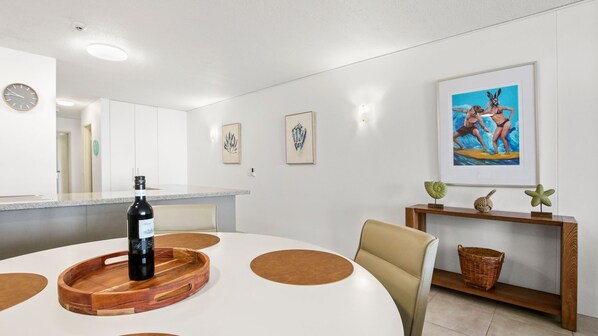A modern dining area with a round table, a bottle of wine, and a framed picture on the wall. - Seapoint Unit 14, 32 Victoria Tce, Kings Beach (Kings Beach)
