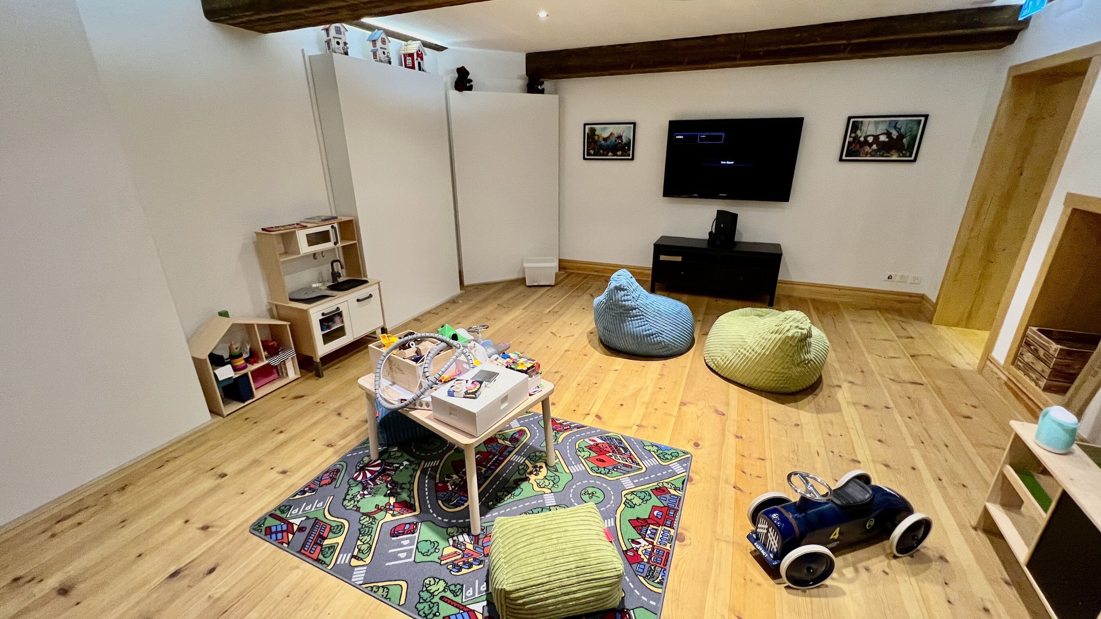 A child's playroom with a play table, bean bags, a toy train, and a television on the wall.