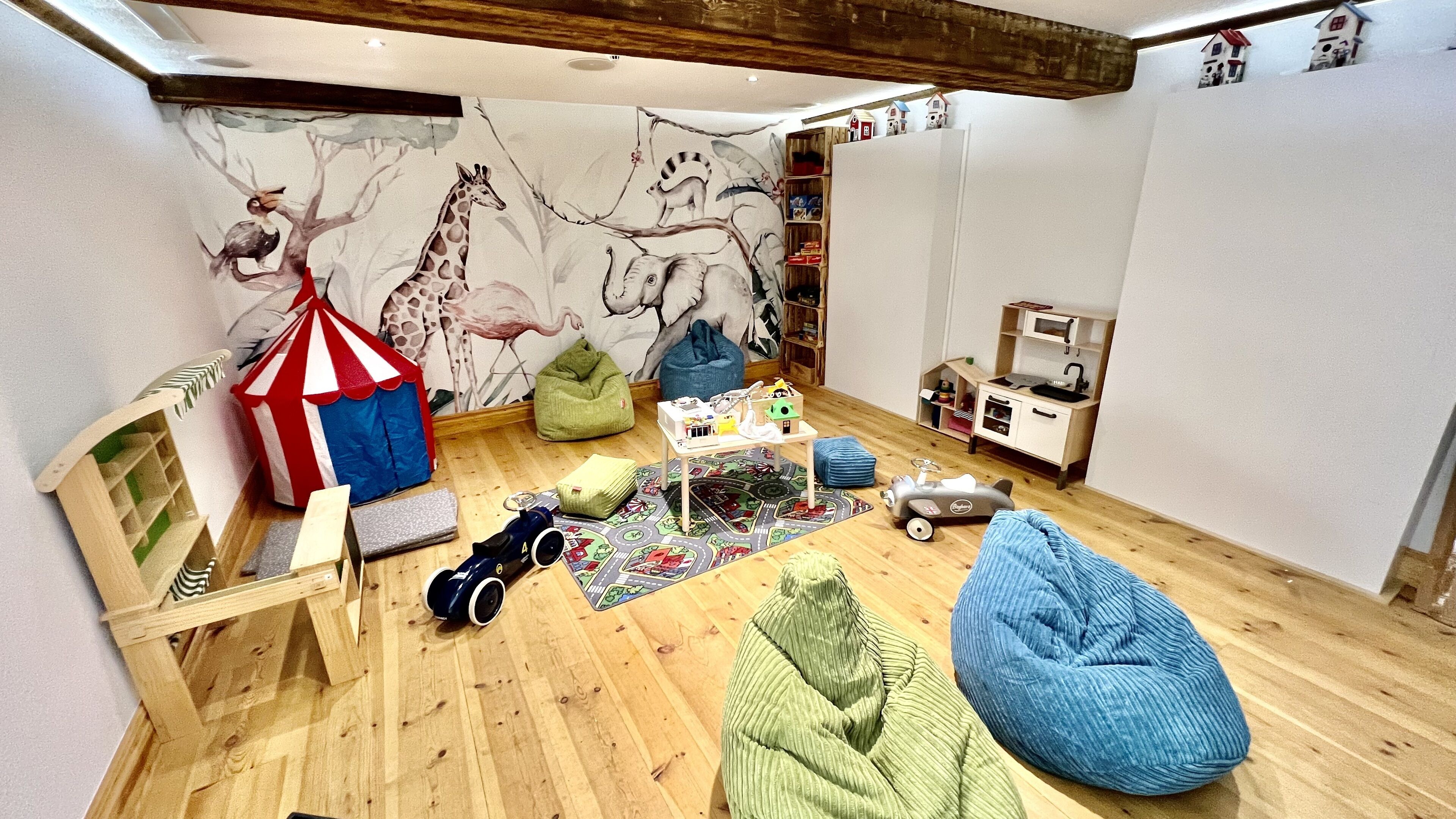 A child's playroom with a wooden floor, a mural of animals, a play table, and a toy kitchen set.