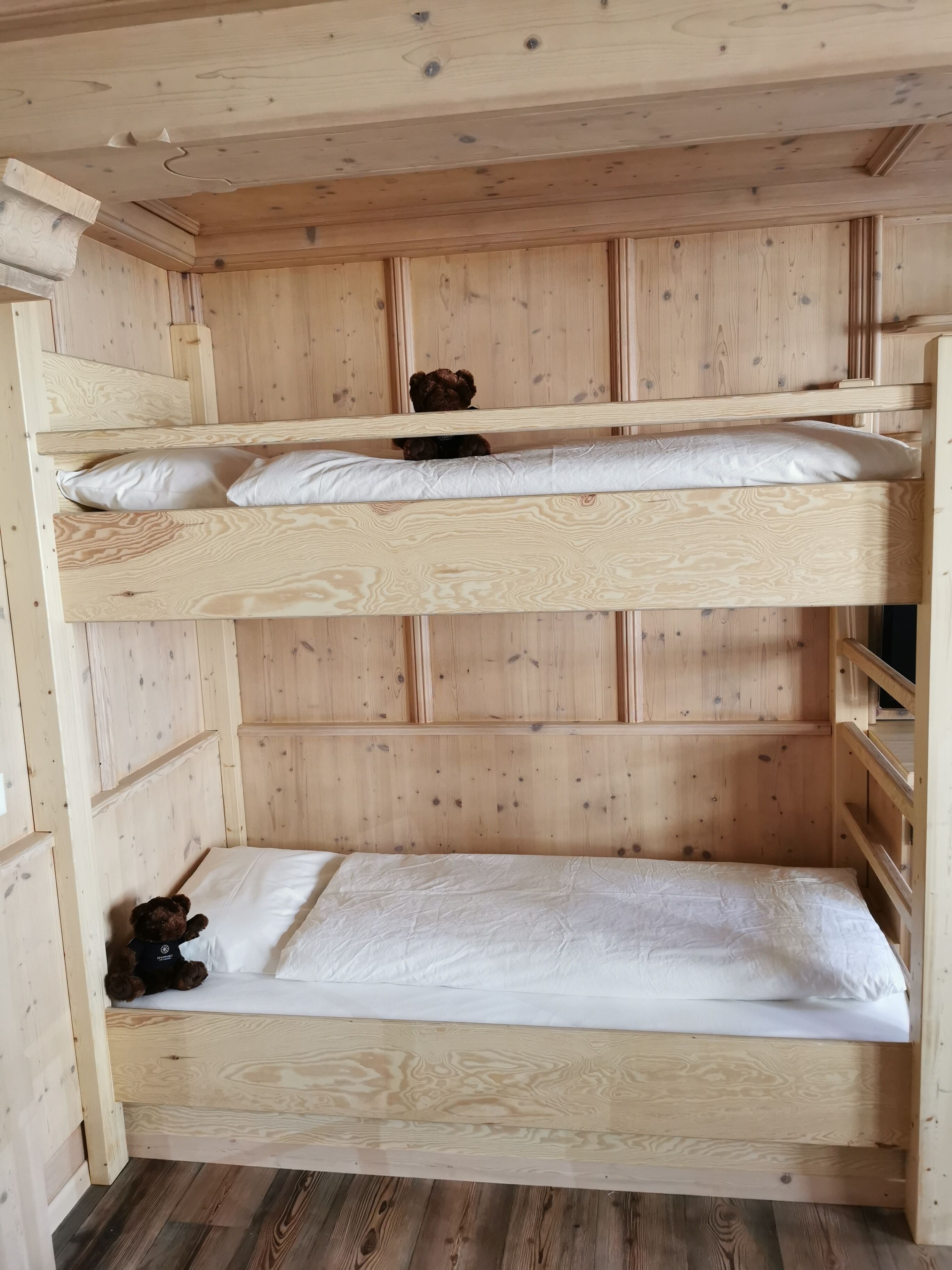 Een stapelbed met twee niveaus, elk voorzien van een kussen en een teddybeer.