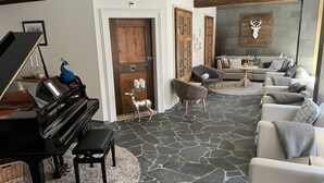 A living room with a grand piano, a stone floor, a sofa set, and a deer sculpture.