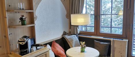 Una habitación acogedora con interior de madera, un sofá con cojines, una mesita y una ventana con vistas a árboles cubiertos de nieve.